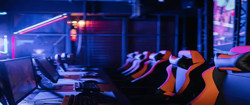 Rząd wysokowydajnych stanowisk do gier z klawiaturami RGB, monitorami do gier i ergonomicznymi fotelami w profesjonalnym klubie gier komputerowych.